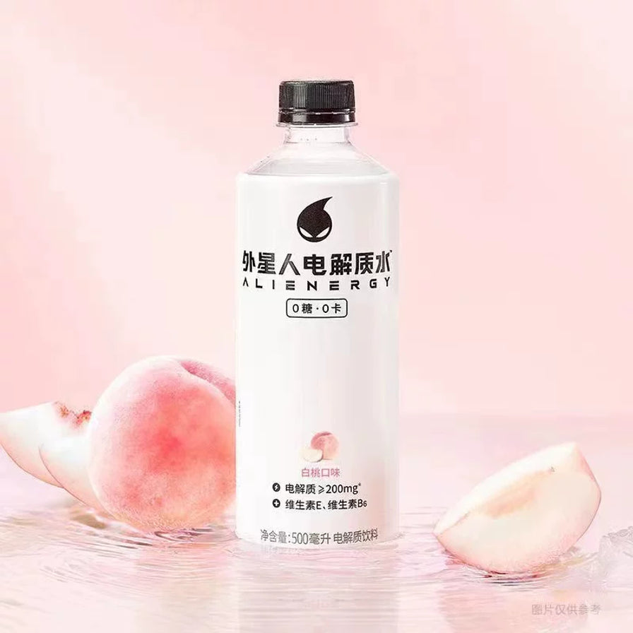 外星人电解质水白桃口味，瓶身置于粉色背景中，周围点缀有新鲜白桃切片和水波纹。