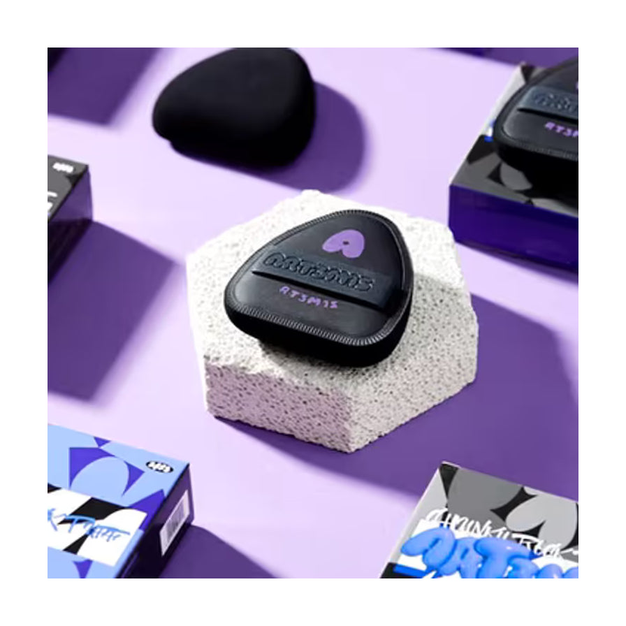 ART3MIS 黑墩墩粉扑静物场景图，产品置于白色石块上，背景为紫色调并伴有包装盒元素。