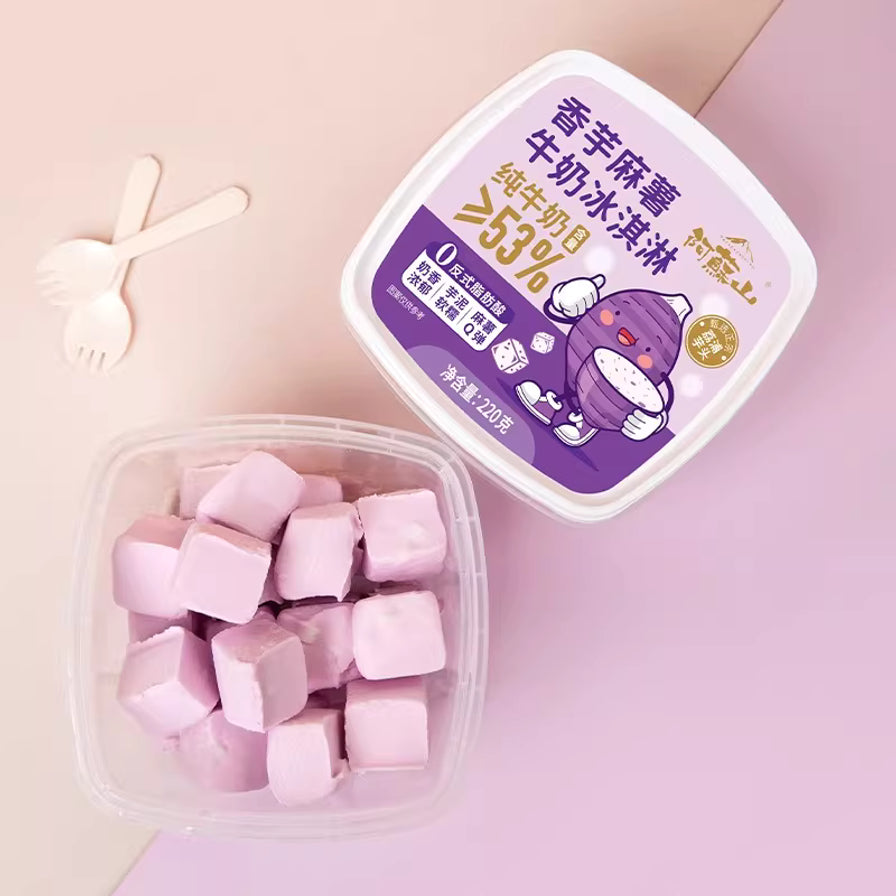俯拍视角展示阿苏山香芋麻薯牛奶冰淇淋，包含紫色包装盒及盒内淡紫色小方块造型的雪糕，旁边配有小勺。