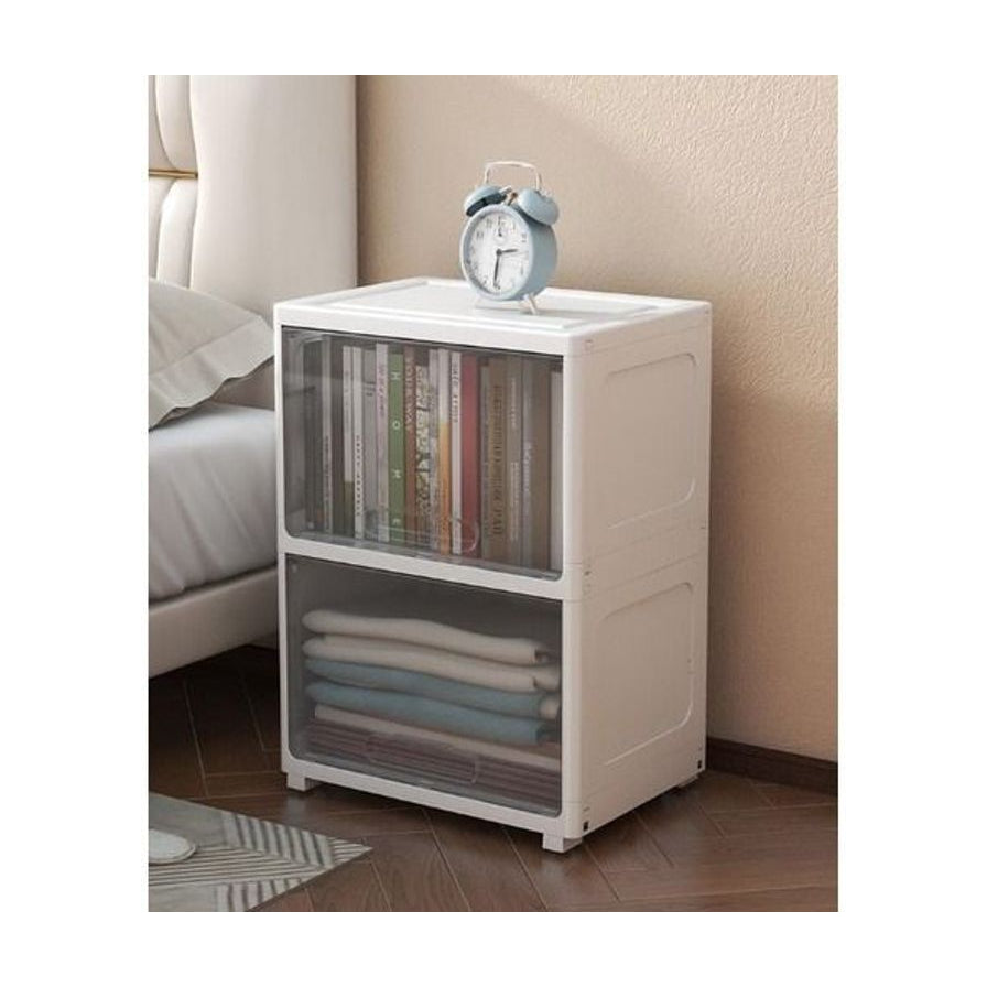 白色双层收纳柜放置在卧室床边，顶部放有蓝色闹钟，展示家居使用场景。