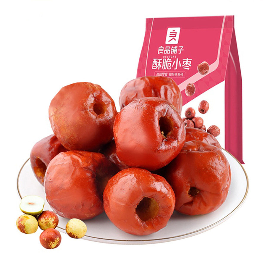 白盘中堆叠的良品铺子去核酥脆小枣近景，背景为红色商品包装袋