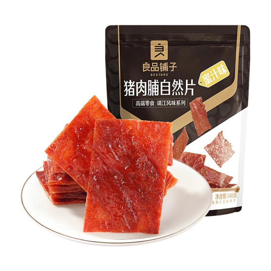良品铺子蜜汁猪肉脯，白色圆盘中整齐叠放的红色肉脯，背景为黑色包装袋，标注有蜜汁味和靖江风味系列。