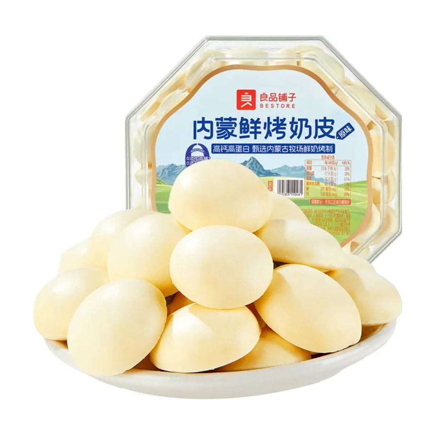 良品铺子内蒙鲜烤奶皮产品特写，白色盘中堆叠着多枚淡黄色圆形奶片，背景为竖立的八角形包装盒。