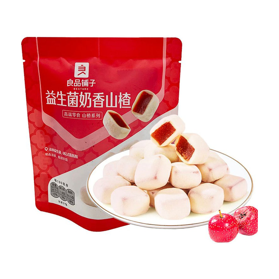 良品铺子益生菌奶香山楂红色包装袋，前方白色瓷盘盛满奶白色外皮、红色山楂内芯的方块果脯，右下角点缀两颗新鲜红山楂。