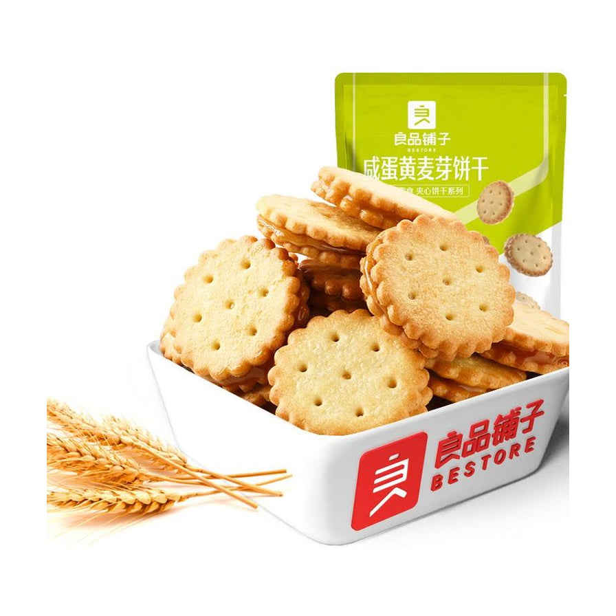 盛放在白色方碗中的良品铺子咸蛋黄麦芽饼干，碗侧印有品牌Logo，背景为产品包装。