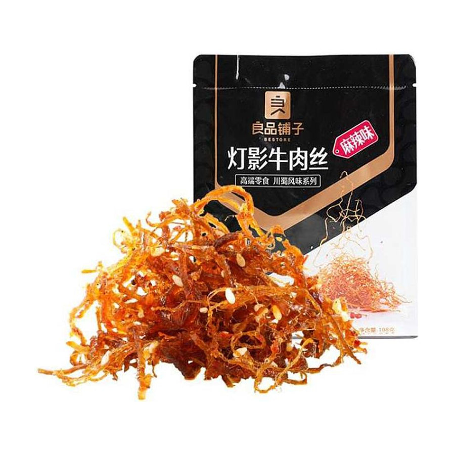 良品铺子麻辣味灯影牛肉丝，包装袋前堆叠着裹满芝麻、香辣诱人的牛肉细丝，展示出紧实的肉质纹理。
