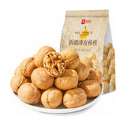 良品铺子新疆薄皮核桃，白色圆盘中堆叠着饱满的核桃，其中一颗已剥开露出完整果仁，背景为产品包装袋。