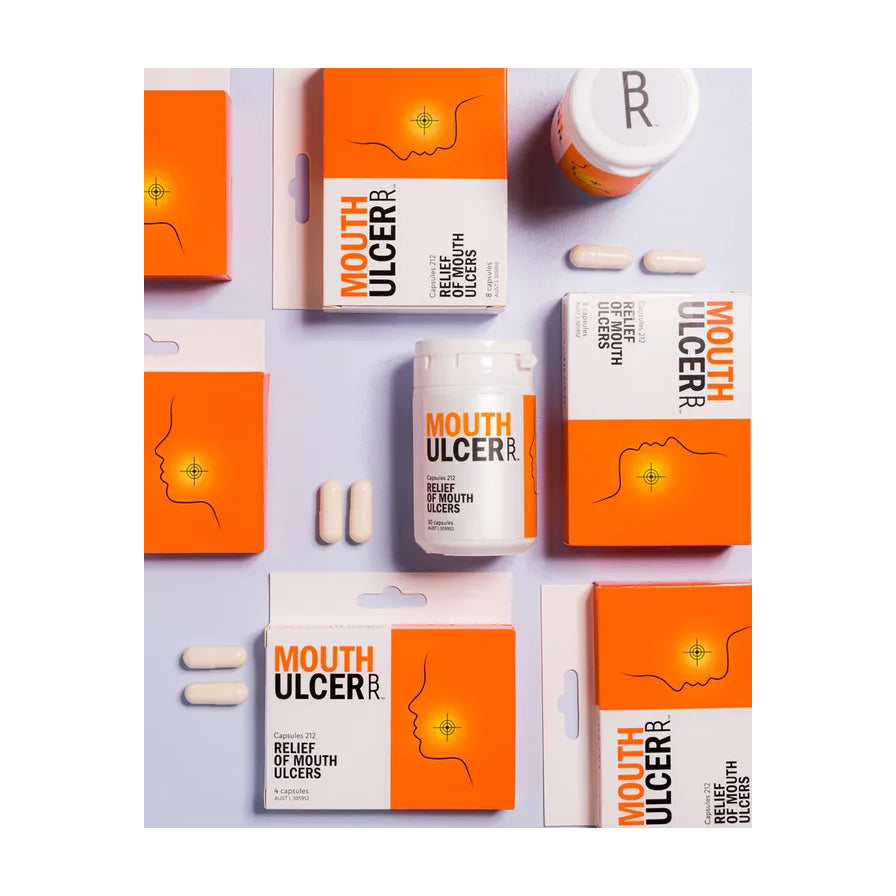 多盒 BioRevive 口腔溃疡修复胶囊与散落的白色胶囊在紫色背景上的俯视图。