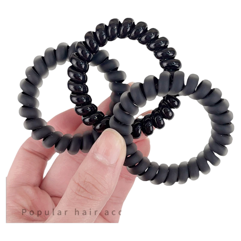 一只手拿着三个黑色螺旋电话线发圈，展示其高弹力材质和纹理细节。