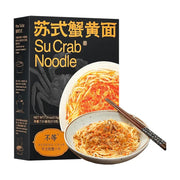不等苏式蟹黄面黑金版包装盒与成品展示，黑色盒身印有金色中英文字样及食用方式图示，前方摆放一碗拌好蟹粉的面条和一双筷子。