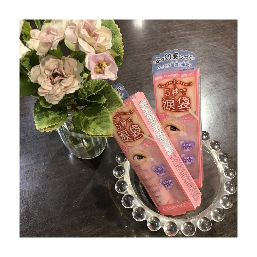 Canmake Tokyo 卧蚕笔产品包装摆放在玻璃托盘上，背景配有粉色花朵装饰的生活场景图。