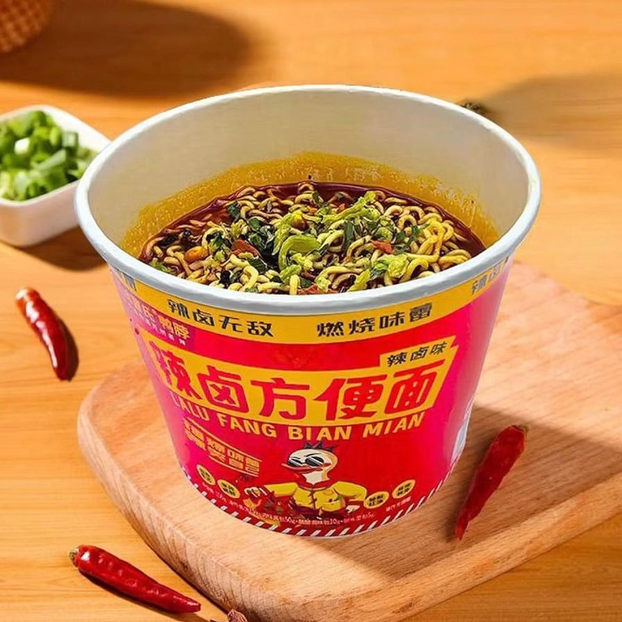 冲泡好的曹氏鸭脖辣卤方便面，面条浸泡在浓郁的红油汤底中，配有翠绿的蔬菜，放置在木质托盘上。