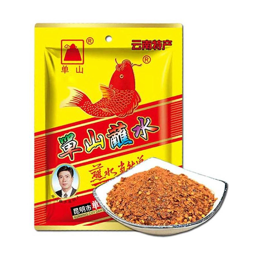单山蘸水黄色包装袋，印有红色鲤鱼图案，前方摆放一碟红色的干碟辣椒面调味料。