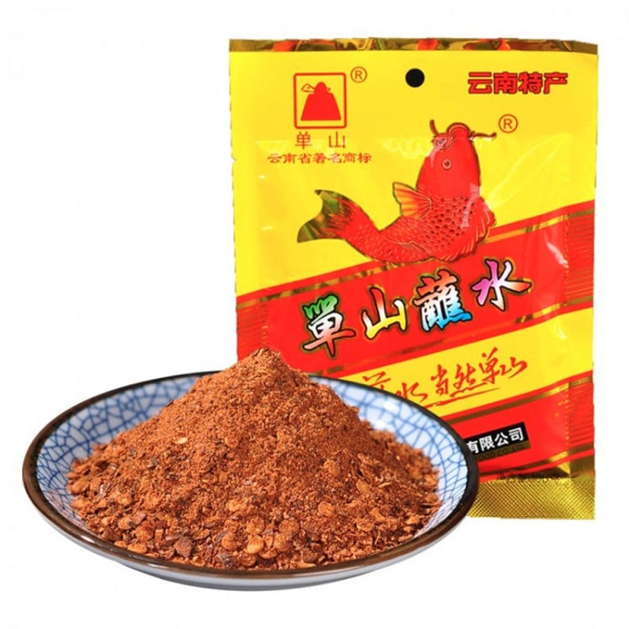 单山原味蘸水黄色包装袋，印有红色锦鲤图案，前方是一碟堆成小山状的深红色辣椒面。