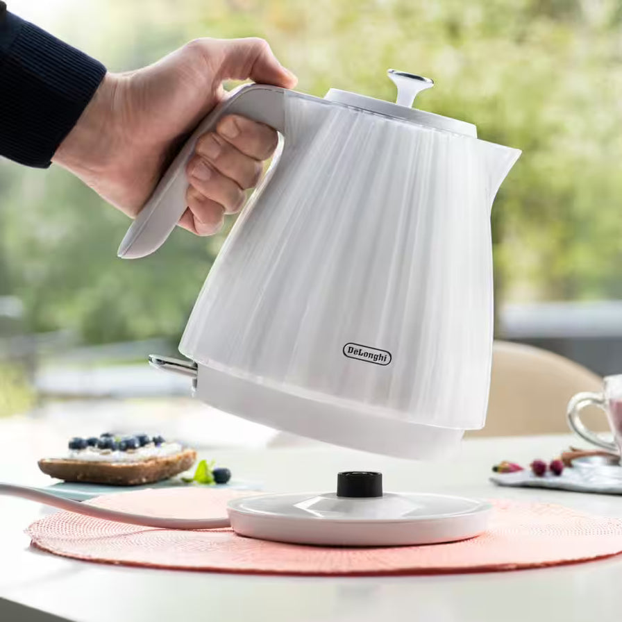 手持 De'Longhi 德龙 Ballerina 电热水壶从底座取下的使用场景图，展示 360 度旋转底座。