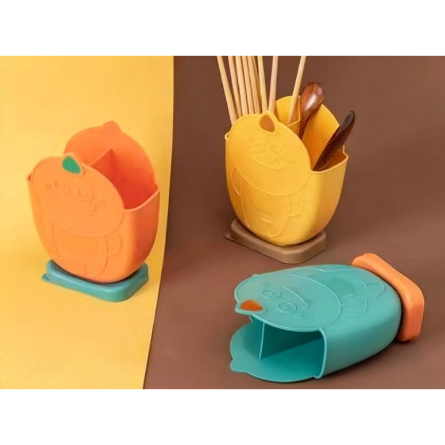 三款不同颜色的恐龙造型筷笼展示，包含橙色、黄色和青绿色，其中黄色款内插有木质筷子和勺子，展示实际收纳效果。