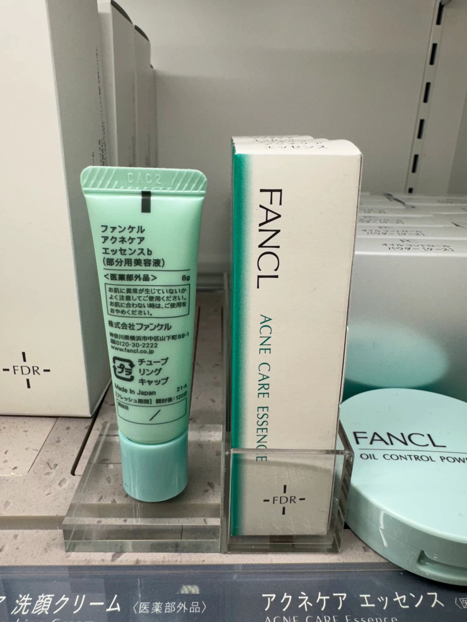 Fancl 祛痘凝露实物手持特写，展示管体细节与背景环境