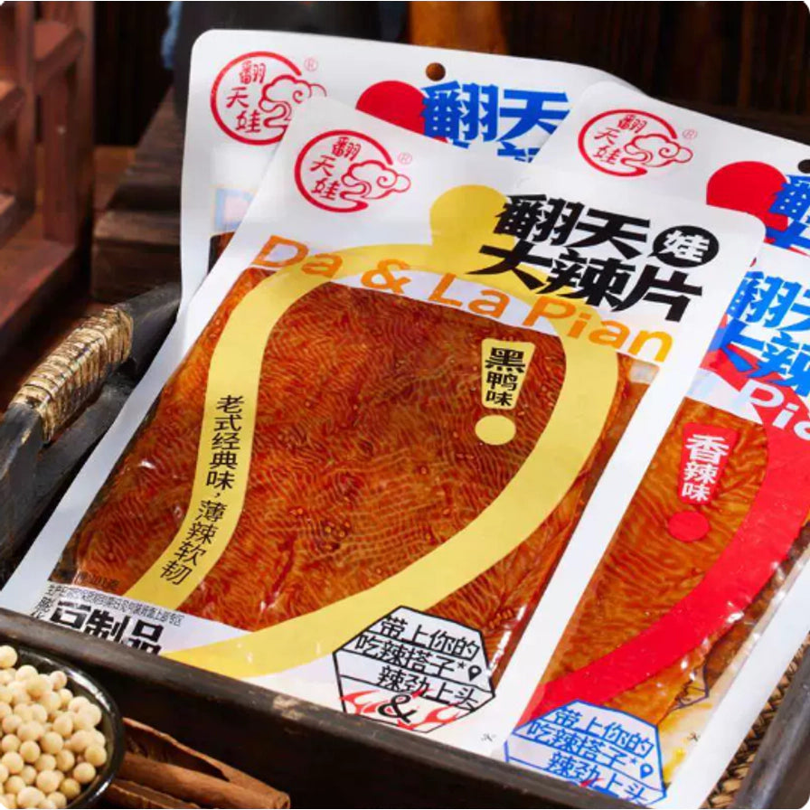 翻天娃大辣片黑鸭味与香辣味包装斜放展示，背景为木质托盘和黄豆，突出怀旧零食质感。
