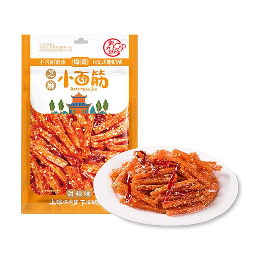 翻天娃芝麻小面筋甜辣味包装袋，前方白色圆盘盛放着裹满芝麻和辣椒丝的条状辣条。
