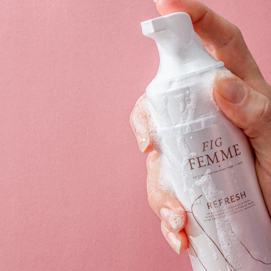 手持 FIG FEMME 私处清洗泡沫瓶身，泵头处有绵密白色泡沫，粉色背景