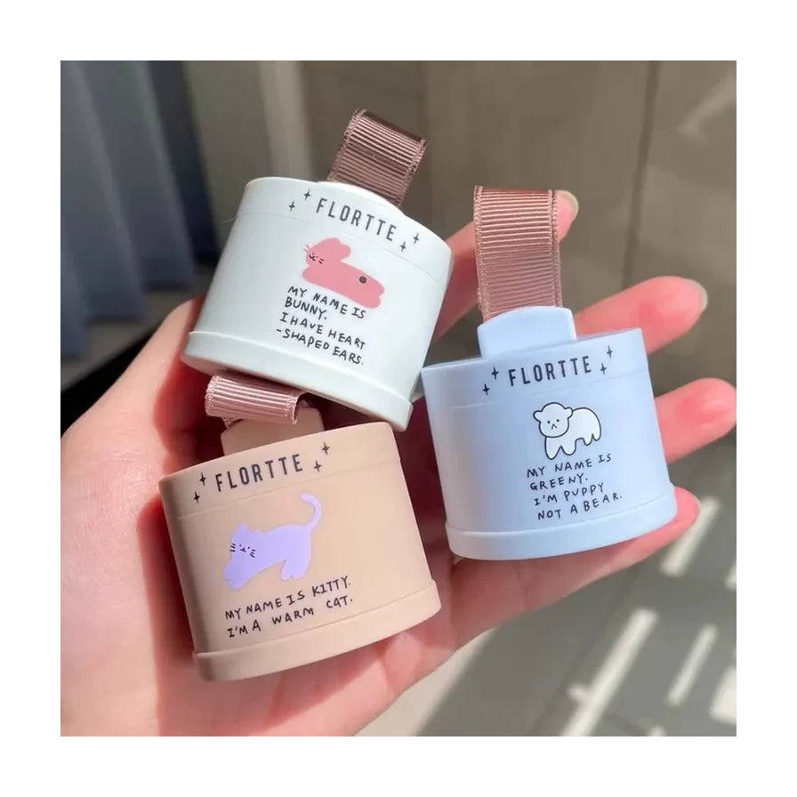 一只手拿着三款 FLORTTE 碎碎念系列发际线粉，分别为白色、浅蓝色和米色包装，展示不同颜色的可爱动物图案设计。