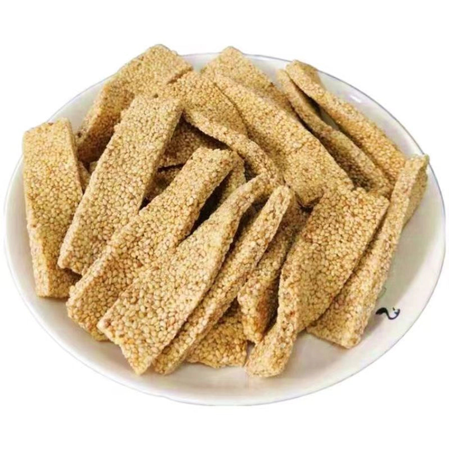 一盘手工白麻糖，长条状的麻糖表面布满芝麻，层叠摆放在白色花边圆盘中。