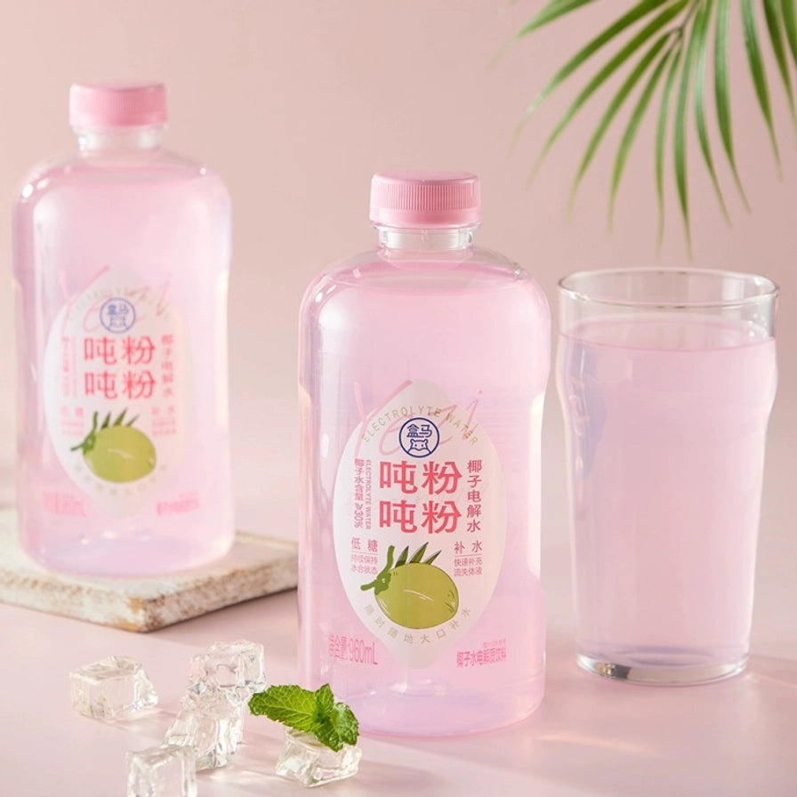 两瓶盒马吨吨粉粉椰子电解水与一杯倒入杯中的粉色饮品，配有冰块和薄荷叶装饰。