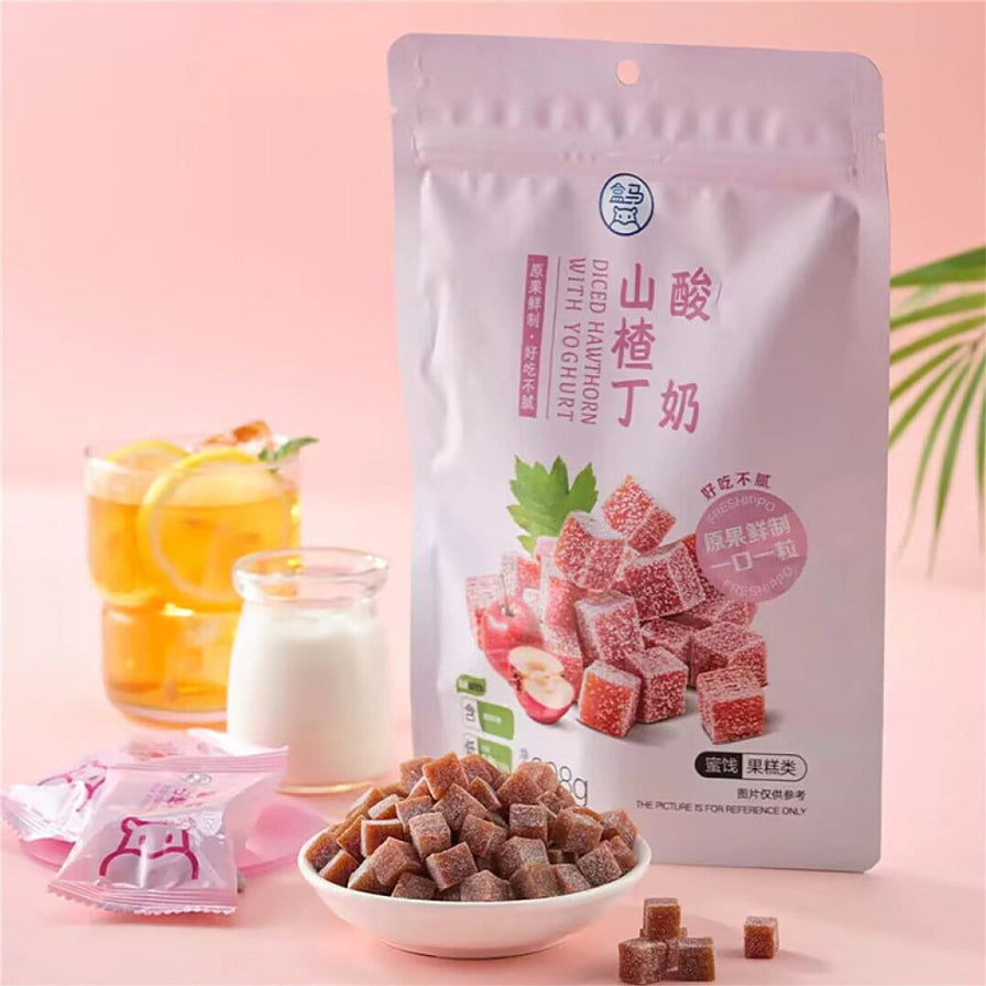 盒马酸奶山楂丁包装袋与散落在碗中的山楂丁，背景配有酸奶和柠檬茶，展示生活化食用场景。