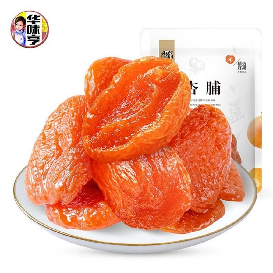 白色圆盘中堆叠的饱满橙色酸杏脯特写，背景为华味亨酸杏脯包装袋，展示果肉厚实有嚼劲的质感。