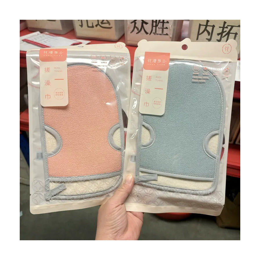 手持展示的两款花漫多双面磨砂搓澡巾，分别为粉色和蓝色，采用透明袋装，背景可见仓库货架。