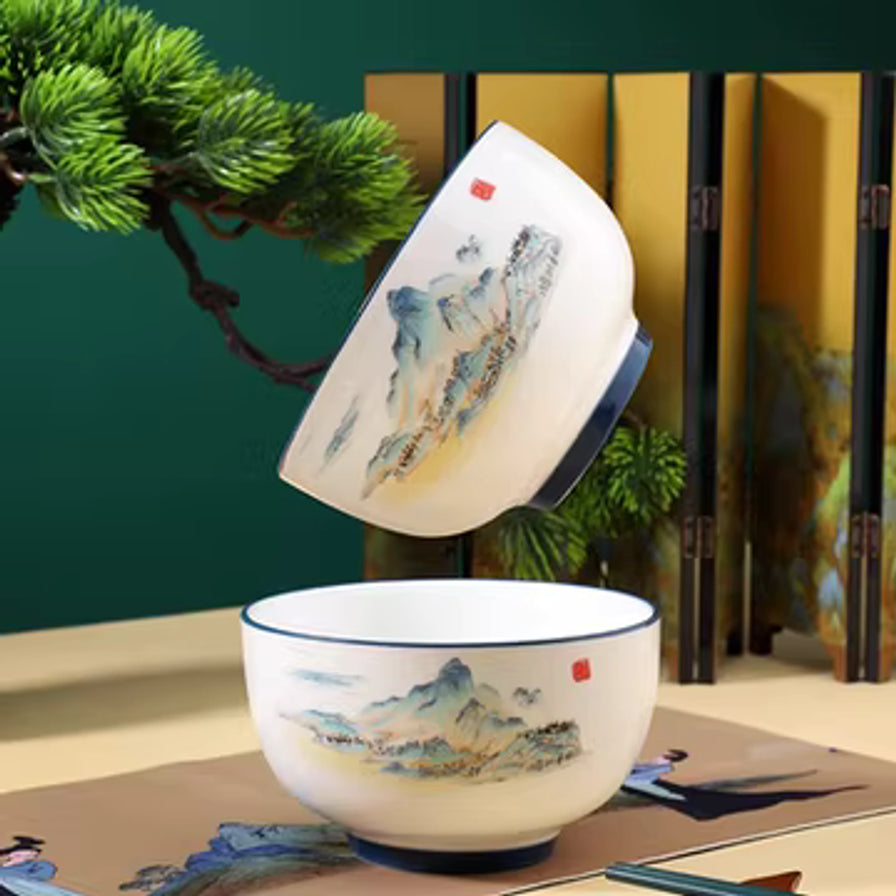 两只日式釉中彩陶瓷面碗在古风背景下展示，一只平放，一只倾斜叠放，背景有松枝和屏风装饰。