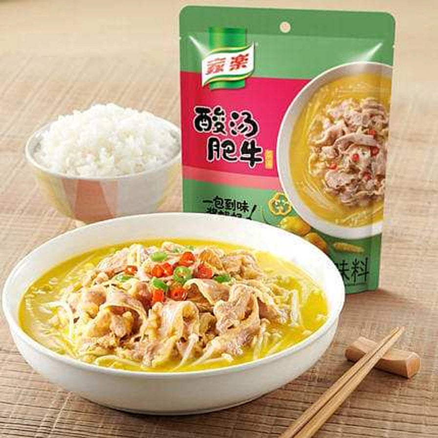 餐桌场景展示：一碗热气腾腾的酸汤肥牛，旁边放着一碗米饭、木质筷子和家乐酸汤肥牛调味料包装袋。