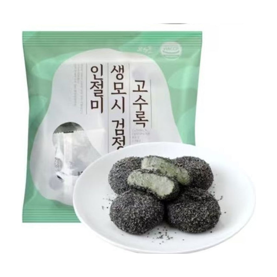 韩国传统艾草黑芝麻麻糬年糕包装袋，前方白色圆盘盛放着裹满黑芝麻碎的绿色麻糬，其中一颗切开展示内部软糯质地。