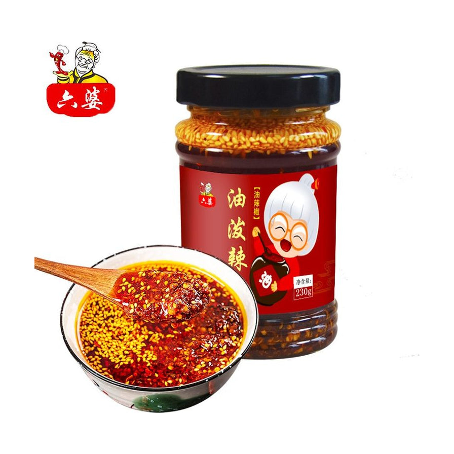 六婆油泼辣子瓶装，前景为一碗盛满红亮辣椒油和芝麻的蘸料，木勺舀起浓郁的辣子。