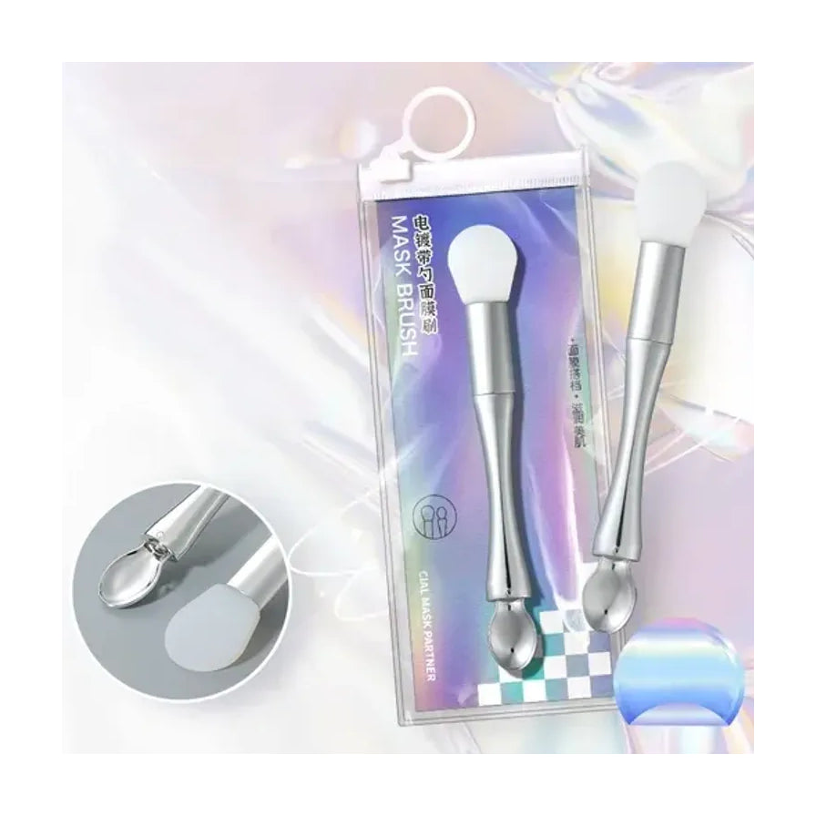 双头面膜刷产品特写，展示银色手柄、白色硅胶刷头及金属勺头细节，背景为镭射包装袋。