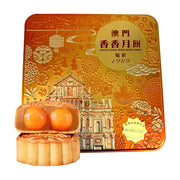 澳门香香双黄白莲蓉月饼礼盒，金色浮雕铁盒包装，前景展示切开的月饼，露出两颗饱满的咸蛋黄。