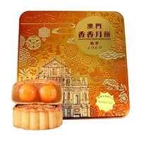澳门香香双黄白莲蓉月饼礼盒，金色浮雕铁盒包装，前景展示切开的月饼，露出两颗饱满的咸蛋黄。