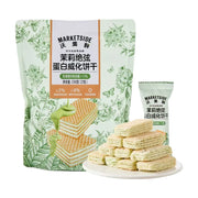 沃集鲜茉莉蛋白威化饼干大袋装与独立小包装，前景为白色圆盘中堆叠的酥脆威化饼干，展示多层夹心结构。