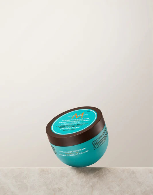 Moroccanoil 强效锁水发膜正面图，深棕色盖子搭配蓝绿色瓶身，置于白色大理石台面上。