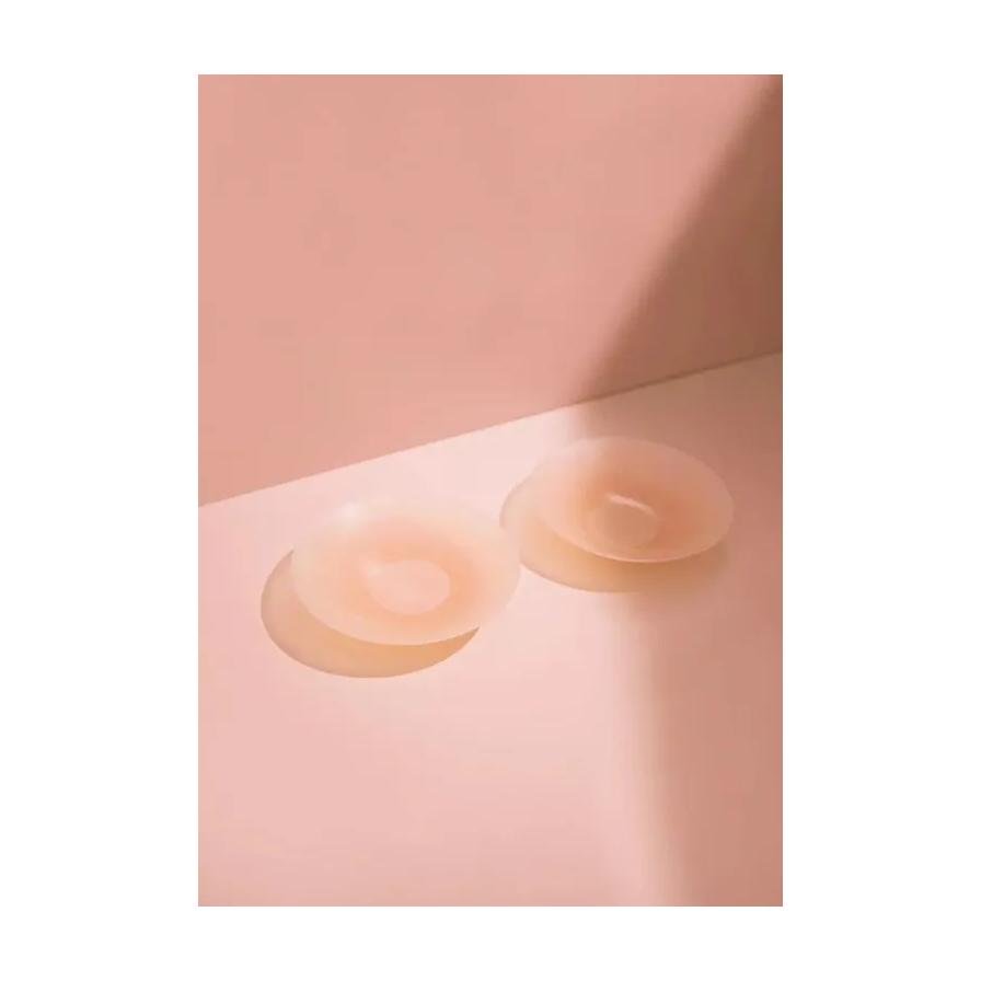 粉色光影背景下展示的两个圆形乳贴侧面特写，呈现中间厚边缘薄的立体结构。