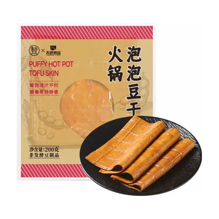 盒马火锅泡泡豆干产品包装与黑色盘中展开的豆皮卷实物展示图，背景为白色。