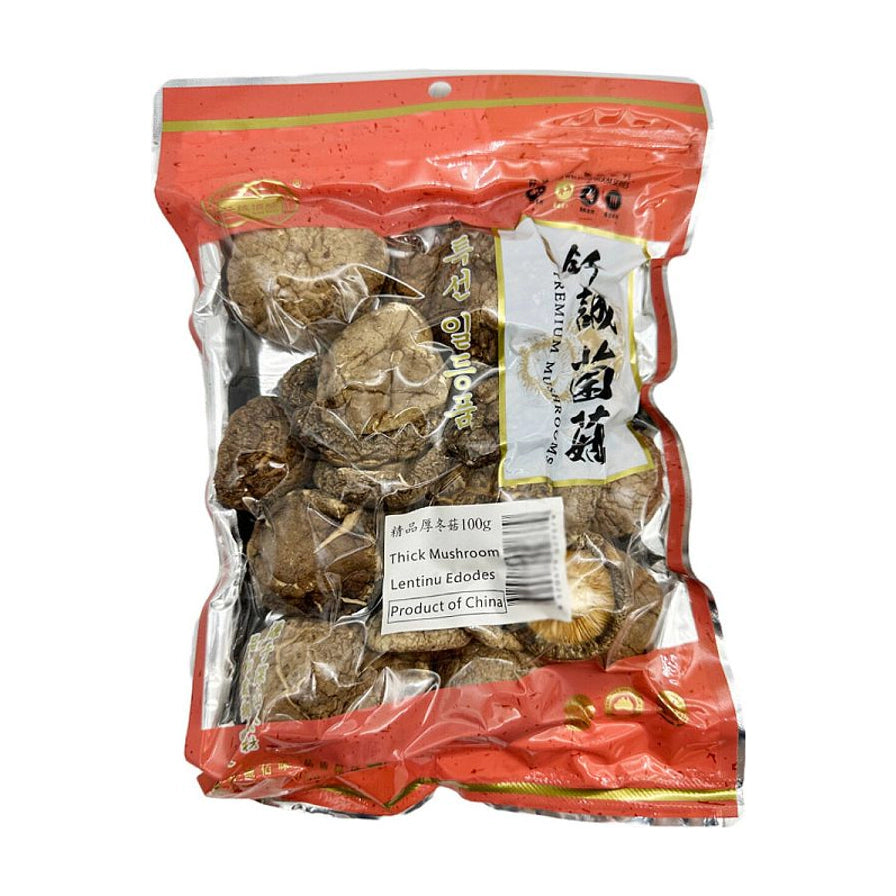 钎诚精品厚冬菇100g包装正面图，透明包装展示内部干燥肥厚的冬菇，背景为木质桌面及竹篮盛放的干香菇。