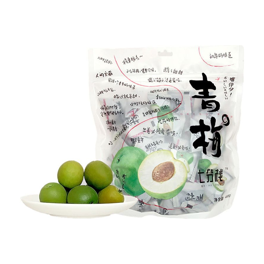七分栈青梅大包装袋，前方白色小碟盛放着数颗新鲜饱满的绿色青梅，包装内含独立小包装。