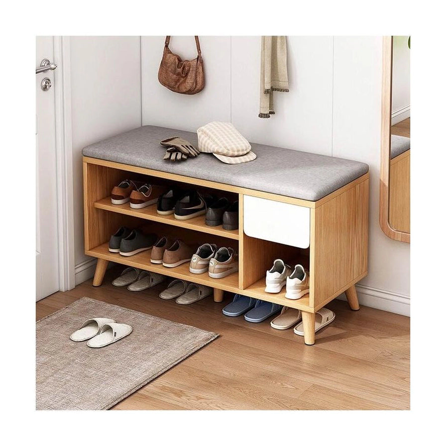 玄关场景中的木质换鞋凳实拍图，放置在门口地垫旁，坐面上放有帽子和手套，下层收纳拖鞋与运动鞋，旁边可见挂包和镜子。