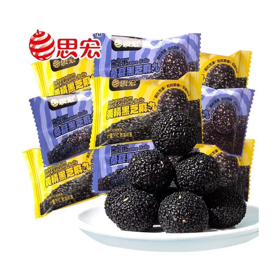 思宏桑葚黑芝麻丸，白色圆盘中盛放着多颗圆润饱满的黑芝麻丸，背景为蓝黄相间的独立小包装袋，包装上印有品牌Logo及产品名称。