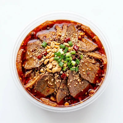 透明圆盒装的川味夫妻肺片成品，红油浸润的牛肉与牛杂切片清晰可见，置于白色背景上。
