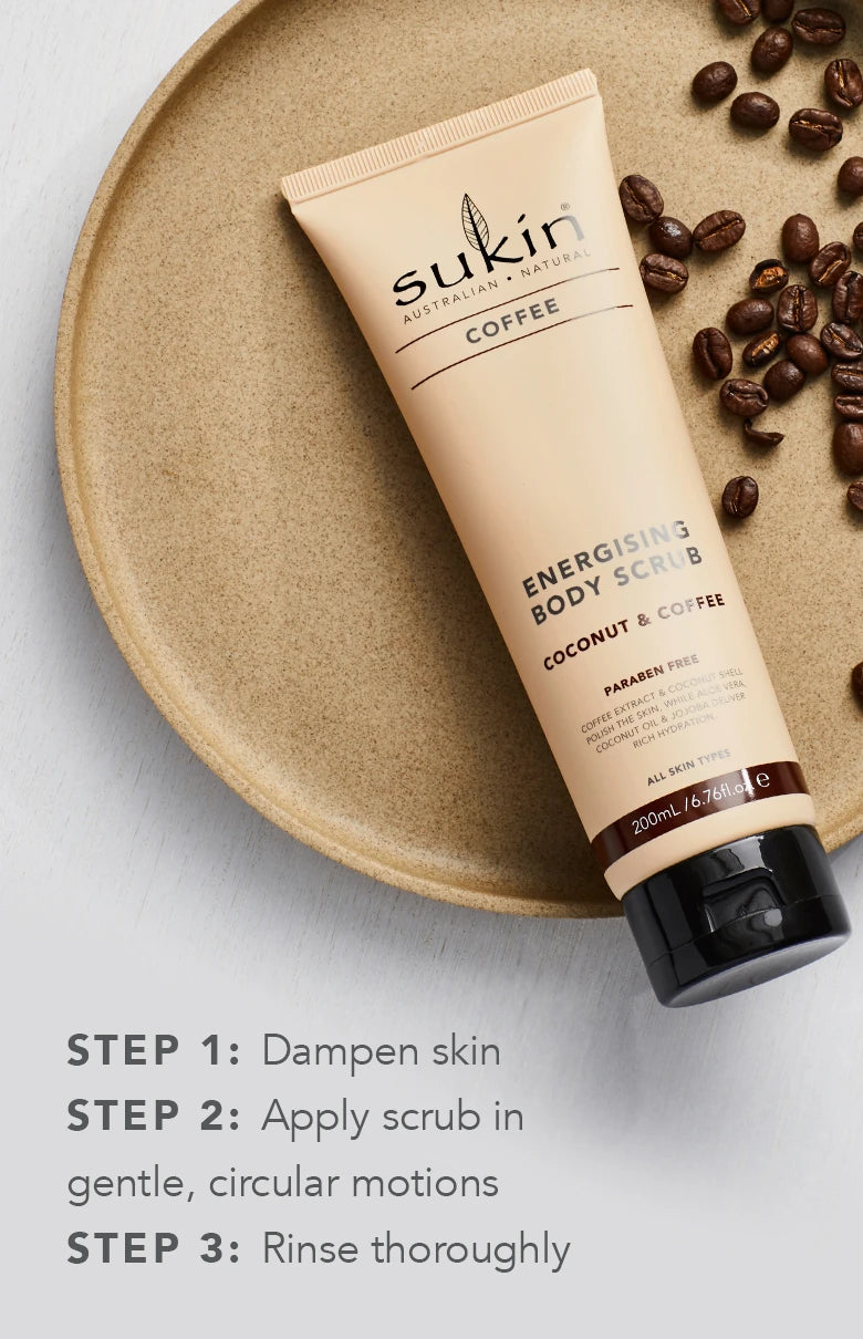 Sukin 磨砂膏置于陶盘上，周围散落咖啡豆，底部配有英文三步使用指南说明。