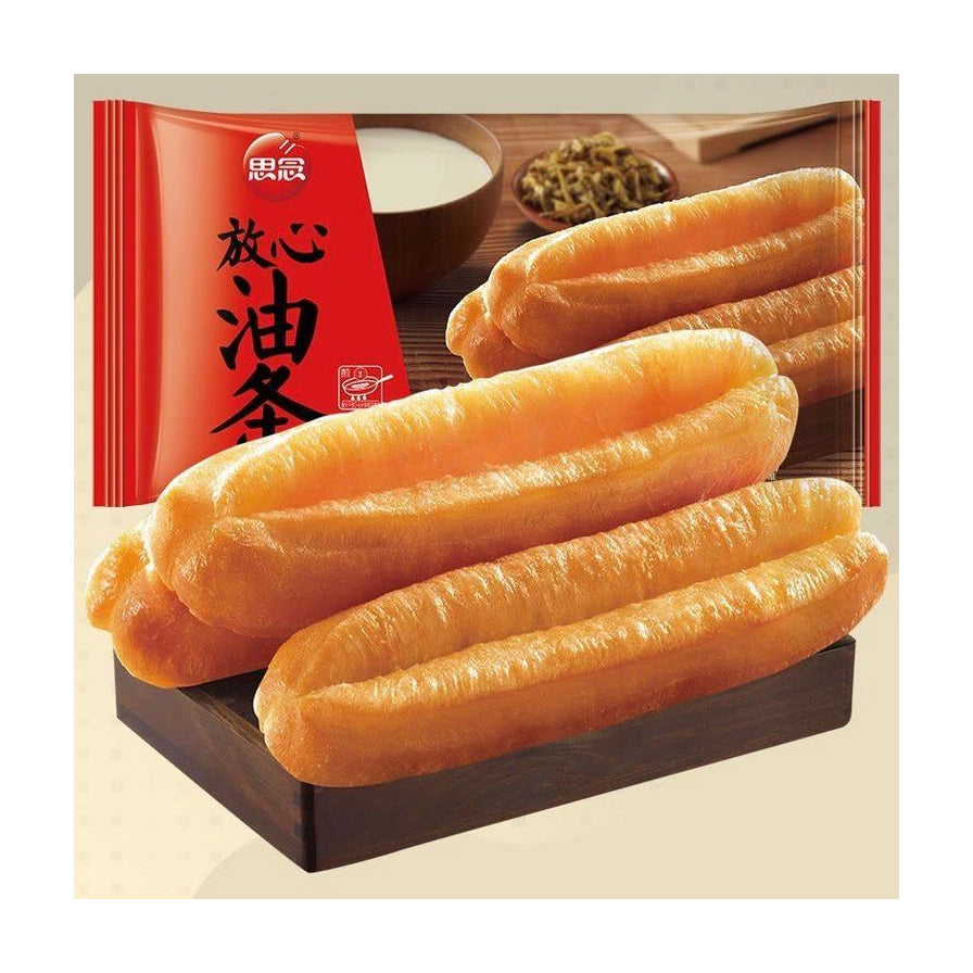 思念放心油条产品特写图，前景为放置在深色木托盘上的几根金黄酥脆油条，背景虚化显示红色产品包装袋。