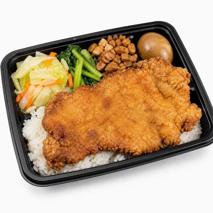 古早大排饭便当，包含一大块金黄酥脆的炸猪排、白米饭、卤蛋、青菜和配菜，采用黑色外带餐盒盛装。