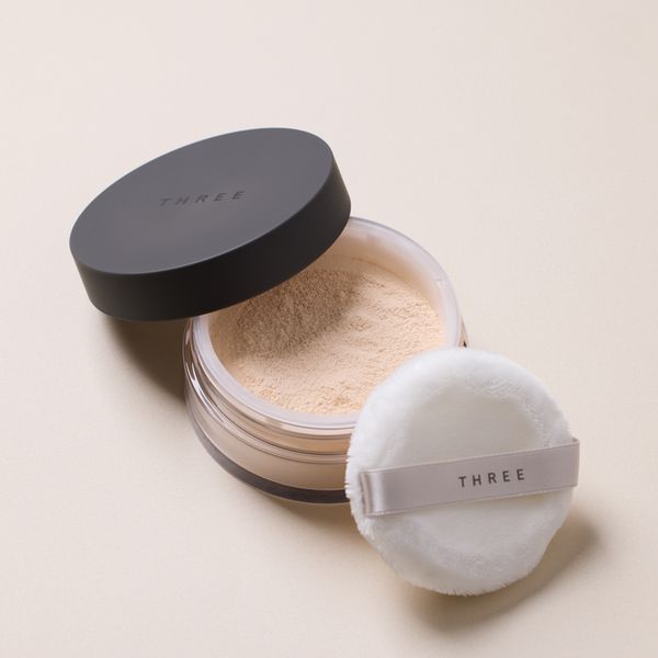Three 凝光蜜粉开盖细节图，展示细腻的粉质和带有品牌 Logo 的粉扑。